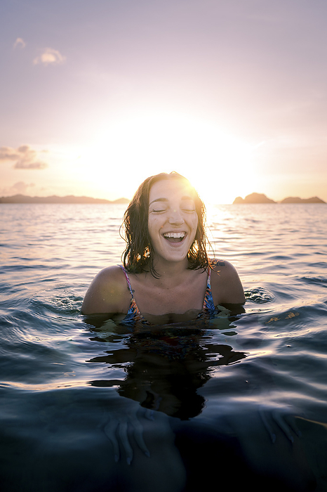Happy woman with eyes closed swimming in sea at sunset