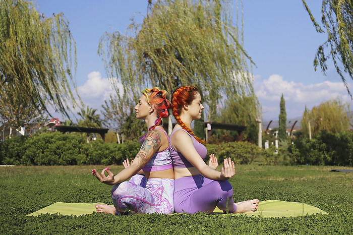 Friends wearing sports clothing meditating on grass in park
