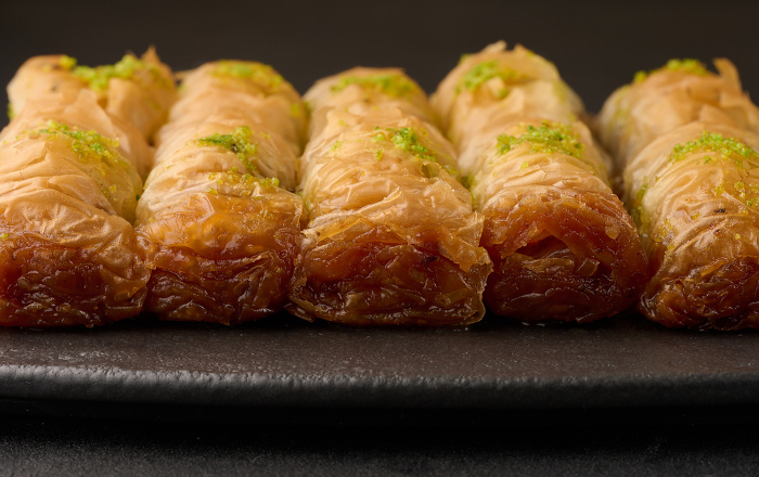 Pieces of baked baklava in honey and sprinkled with pistachios on a black board Pieces of baked baklava in honey and sprinkled with pistachios on a black board