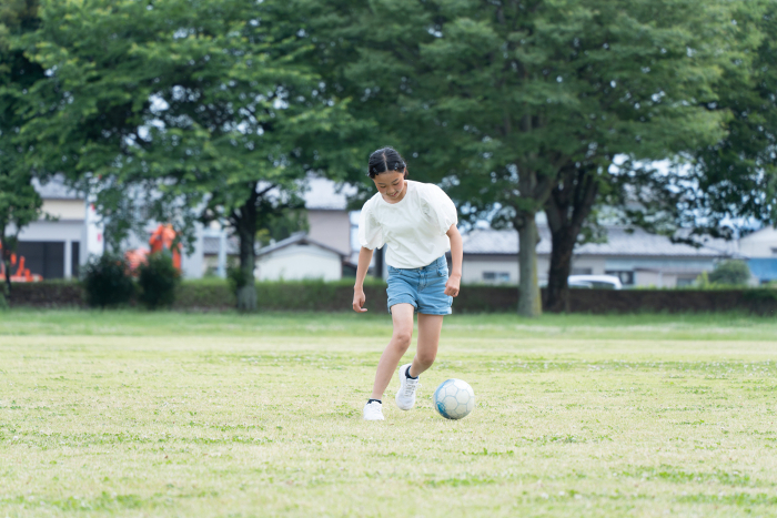 An elementary school girl playing soccer in the park