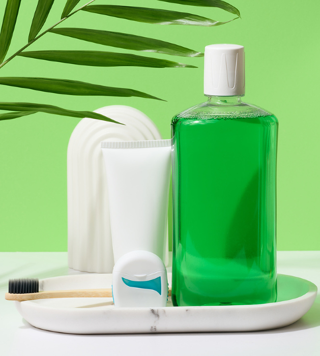 Refreshing mouthwash in a transparent plastic bottle and dental floss, white tube on a green background Refreshing mouthwash in a transparent plastic bottle and dental floss, white tube on a green background