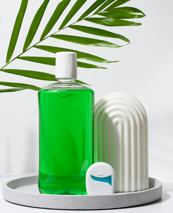 Refreshing mouthwash in a transparent plastic bottle and dental floss on a green background Refreshing mouthwash in a transparent plastic bottle and dental floss on a green background