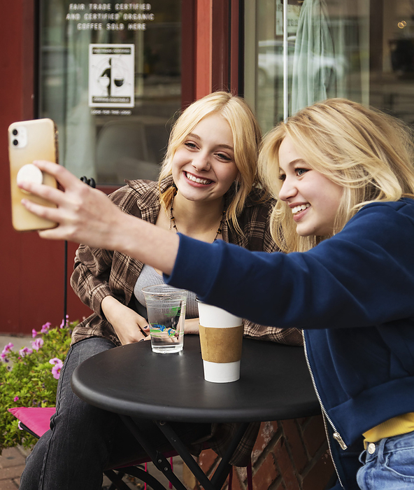 Two teenagers enjoying time together at an outdoor cafe and spending time on their smart phones taking self-portraits; St. Albert, Alberta, Canada, by LJM Photo / Design Pics
