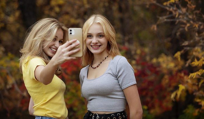 Two teenage girls taking self-portraits with a smart phone while spending time together in a city park on a warm fall day; St. Albert, Alberta, Canada., by LJM Photo / Design Pics