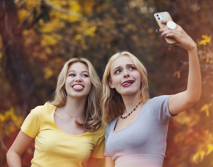 Two teenage girls taking self-portraits with a smart phone while spending time together in a city park on a warm fall day; St. Albert, Alberta, Canada., by LJM Photo / Design Pics