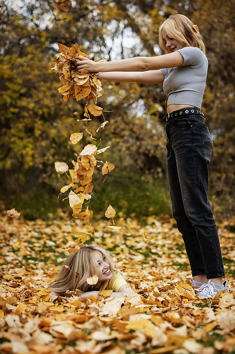 Two teenage girls playing with the leaves and having fun in a city park on a warm fall afternoon; St. Albert, Alberta, Canada., by LJM Photo / Design Pics