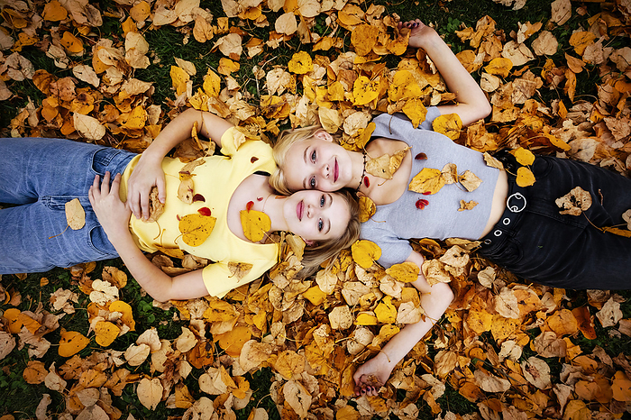 Portrait of two teenage girls laying on the ground in the fallen leaves and looking up at the camera on a warm fall day; St. Albert, Alberta, Canada., by LJM Photo / Design Pics