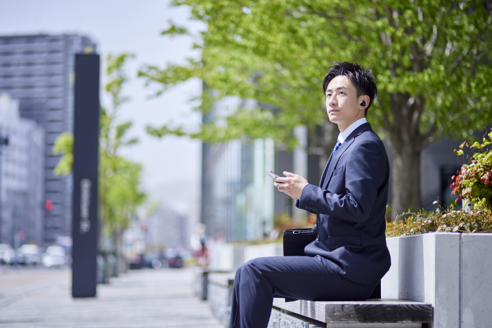 Spring image of a Japanese businessman in his 20s working with wireless earphones and a smartphone (person)