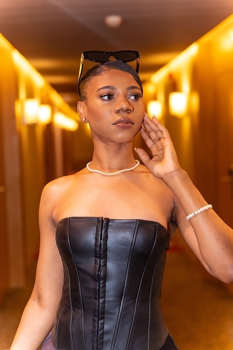 Medium shot of wealthy black ethnic woman posing in hotel room corridor, luxury concept, by Unai Huizi