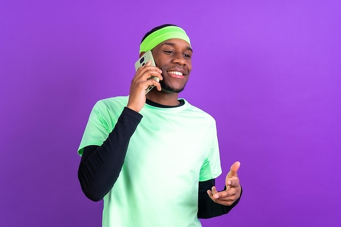 Black ethnic man with a phone in green clothes isolated over purple background, talking on the phone smiling, by Unai Huizi