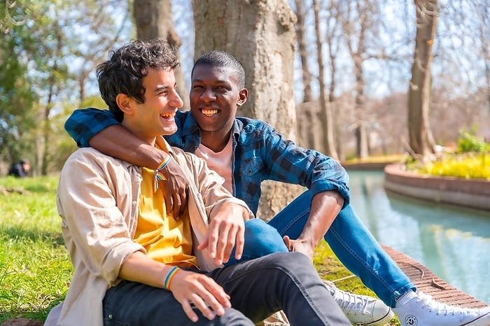 Couple of multiethnic gay men talking quietly in the park, lgbt concept, by Unai Huizi