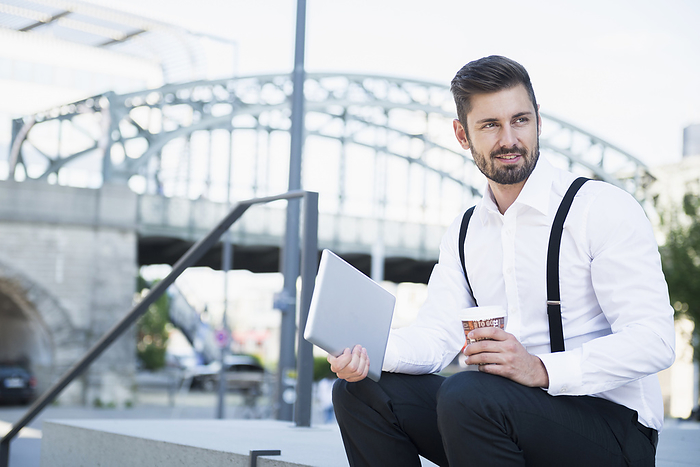 Businessman sitting on the stairs and holding digital tablet with coffee, Munich, Bavaria, Germany Businessman sitting on the stairs and holding digital tablet with coffee, Munich, Bavaria, Germany