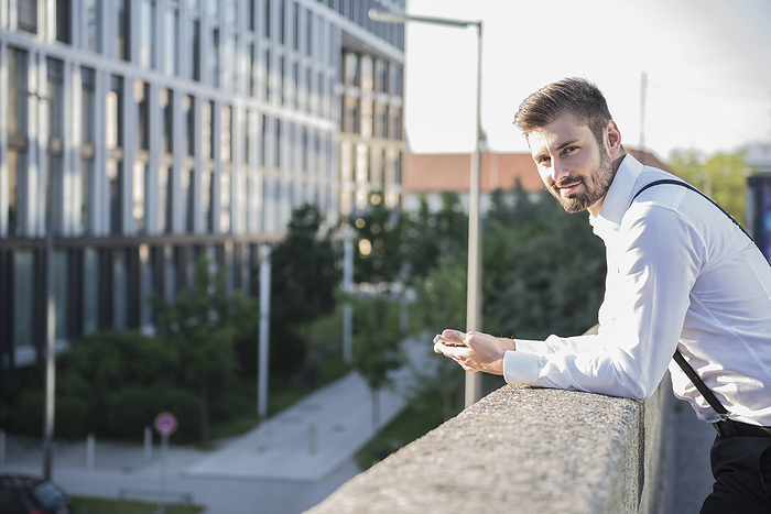 Businessman leaning against railing and holding digital tablet, Munich, Bavaria, Germany Businessman leaning against railing and holding digital tablet, Munich, Bavaria, Germany