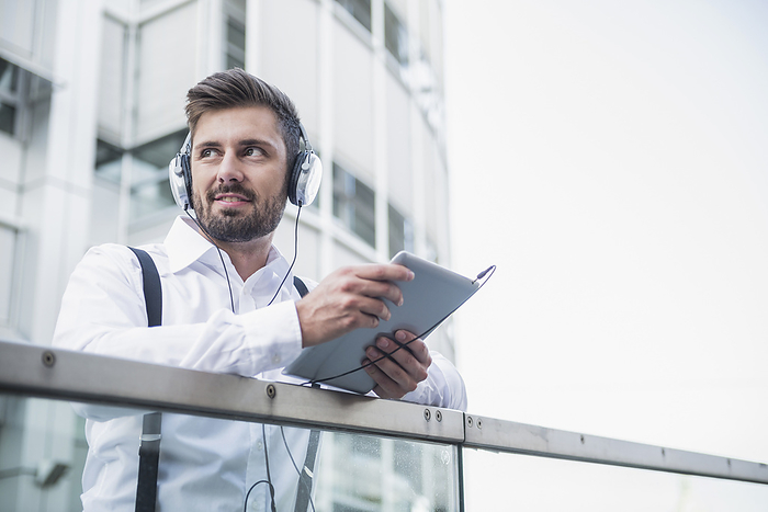 Businessman listening music with headphone in digital tablet, Munich, Bavaria, Germany Businessman listening music with headphone in digital tablet, Munich, Bavaria, Germany