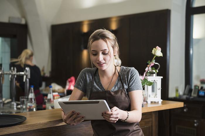 Waitress sitting at the bar and looking at digital tablet, Restaurant, Coffee, Bar, Business entrepreneur  Young woman in apron using tablet at restaurant