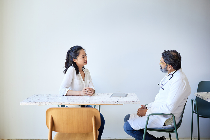 Female patient discussing with male doctor sitting on chair in clinic Female patient discussing with male doctor sitting on chair in clinic