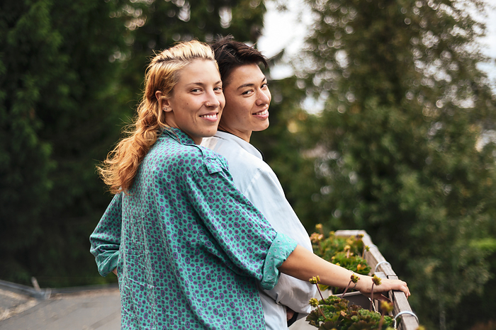 mixed race queer couple stand on balcony with garden smiling