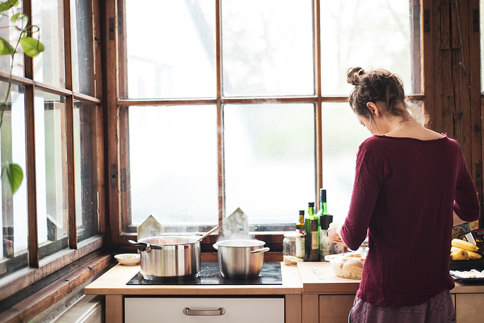 young woman cooks at home in natural wooden kitchen with large window