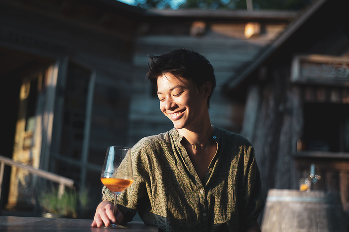 asian person smiles happily with drink in sunlight at wooden cafe