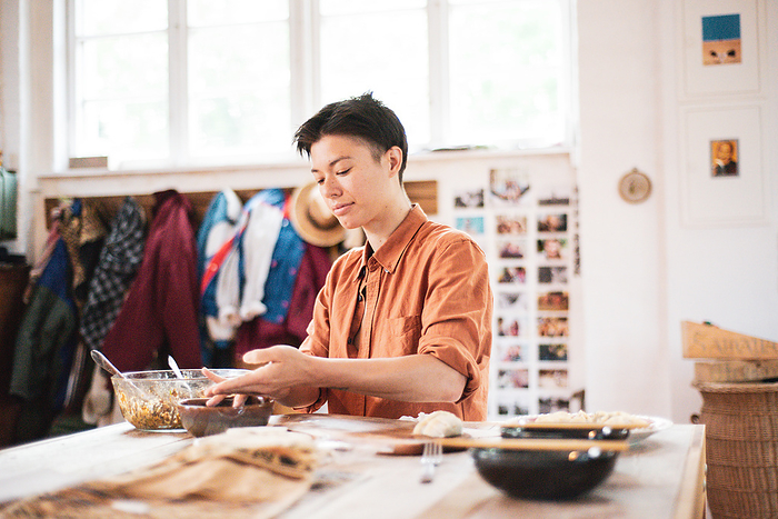 Androgynous asian prepares dumplings on wooden table at home