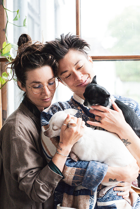 queer couple smile holding their two small dogs together at home