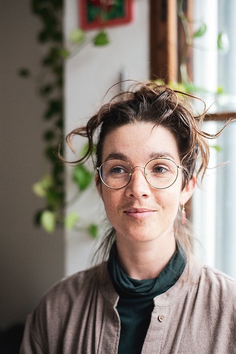 portrait in window of cheeky freckled woman at home with glasses