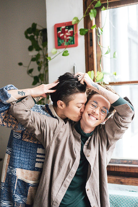 queer couple laugh at play in window light at home with plants