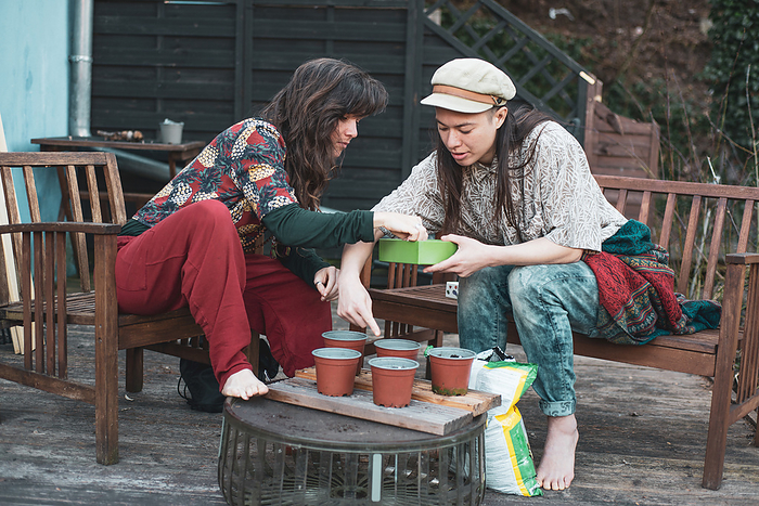 queer female couple plant seedlings in spring on deck