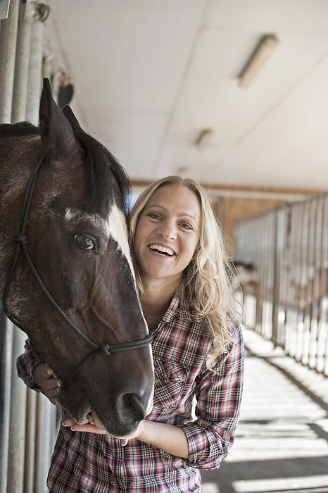 horsewoman with her horse in the stable,horse riding center,liberty,freetime,love to animals, Portrait of a mid adult woman with her horse in barn and smiling, Bavaria, Germany