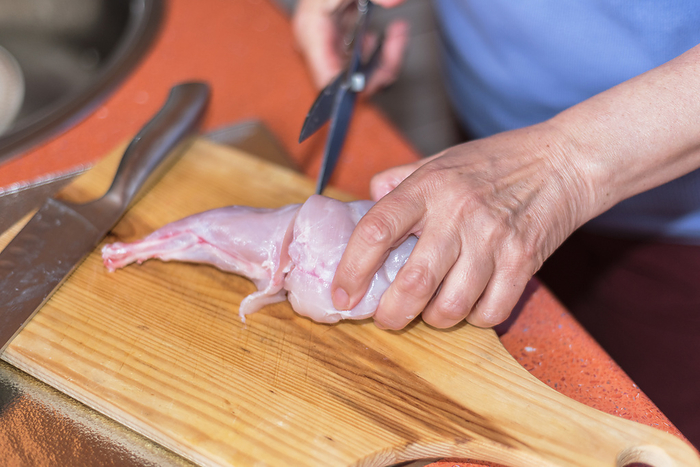 Senior woman hands cutting raw rabbit meat on a wodden table. Shallow dof, selective focus on woman hand. Senior woman hands cutting raw rabbit meat on a wodden table. Shallow dof, selective focus on woman hand., by Zoonar DAVID HERRAEZ