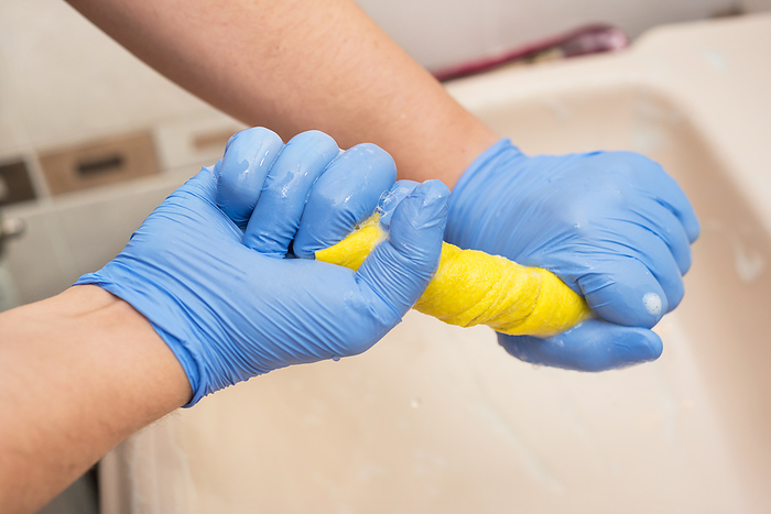 Man cleaning bathroom, draining a sponge cloth Man cleaning bathroom, draining a sponge cloth, by Zoonar DAVID HERRAEZ