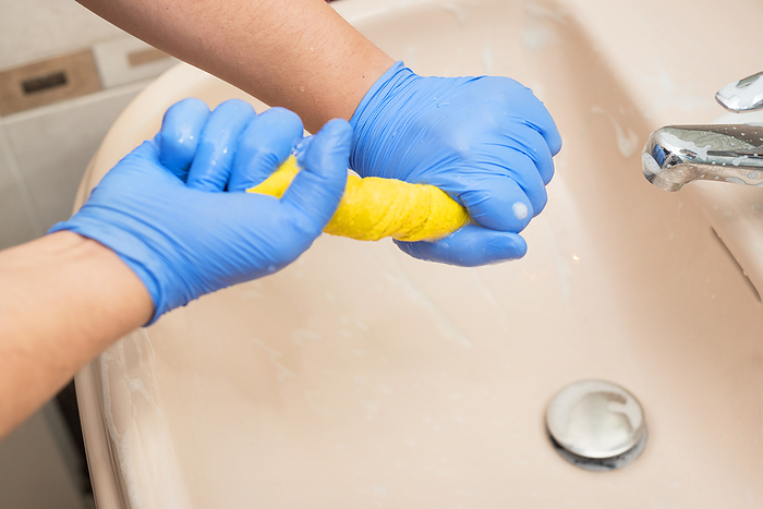 Man cleaning bathroom, draining a sponge cloth Man cleaning bathroom, draining a sponge cloth, by Zoonar DAVID HERRAEZ