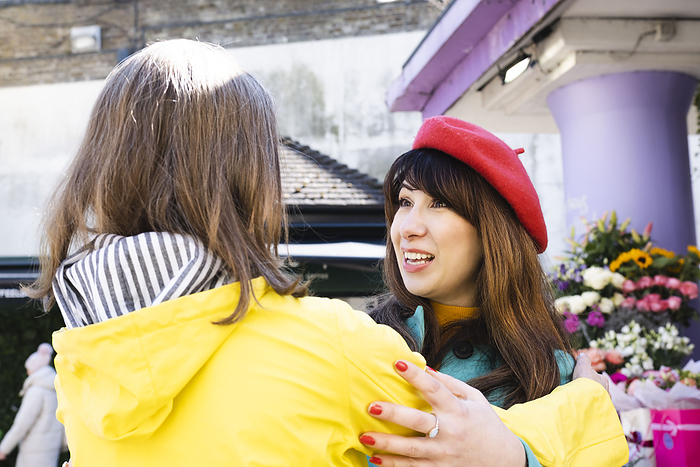 Cheerful woman wearing red beret embracing friend by flower shop
