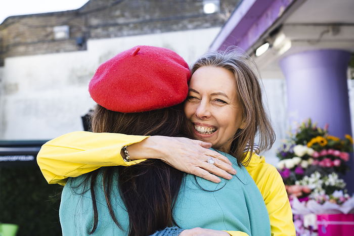 Cheerful mature woman embracing female friend by flower shop