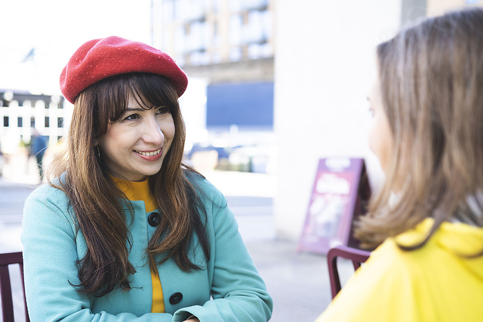 Smiling woman wearing red beret looking at friend at outdoor cafe