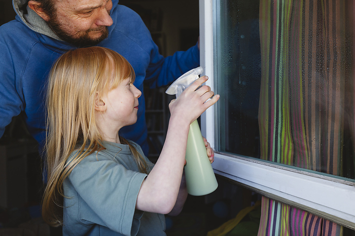 Girl cleaning window with father at home