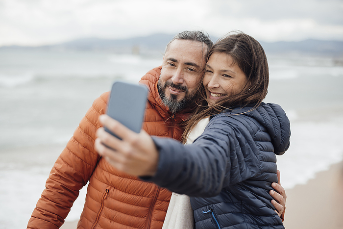 Happy woman taking selfie with man through smart phone at beach