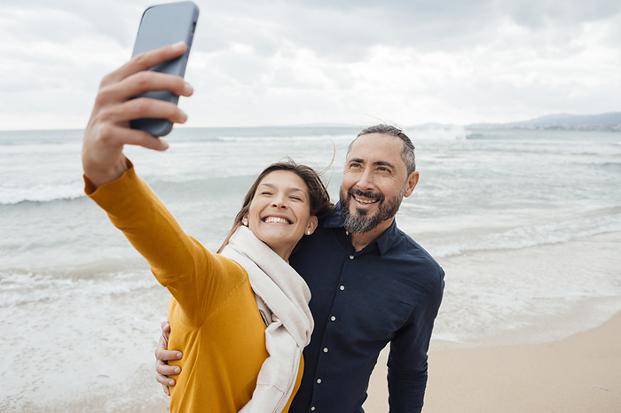 Happy woman taking selfie with man through mobile phone at beach