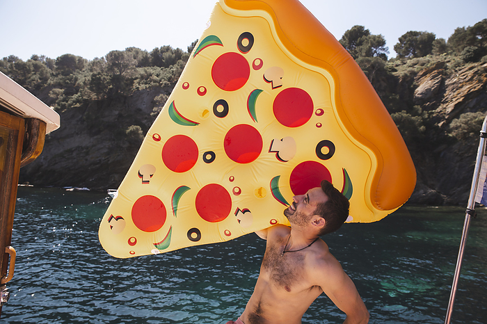 Shirtless man holding pizza shaped air mattress at vacation