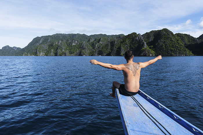 Man with arms outstretched sitting on ship's bow at vacation