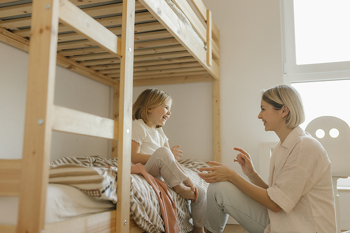 Mother having fun with daughter sitting on bed at home