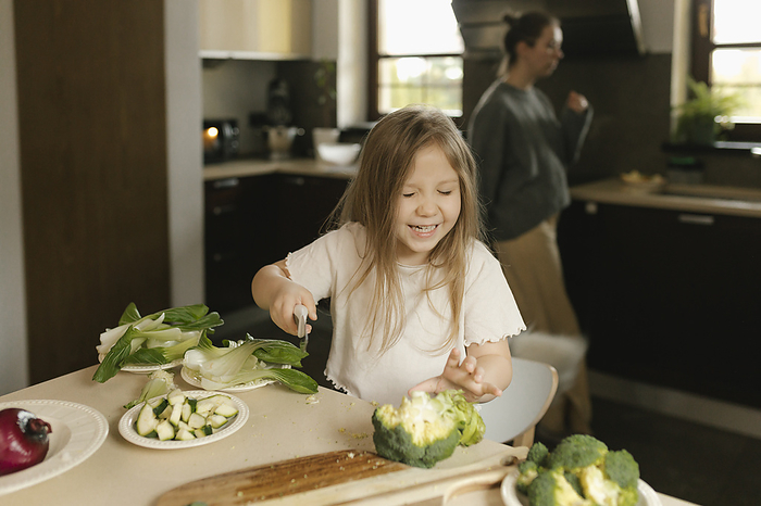 Cheerful girl cutting vegetables in kitchen