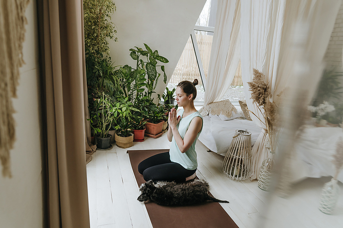 Woman meditating with hands clasped by Schnauzer dog at home