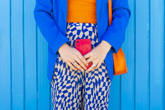 Woman standing holding red smart phone in front of blue wall