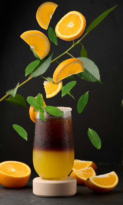 Iced coffee with orange juice in a transparent glass, refreshing bumble coffee on the table. Levitating orange slices and mint leaves Iced coffee with orange juice in a transparent glass, refreshing bumble coffee on the table. Levitating orange slices and mint leaves