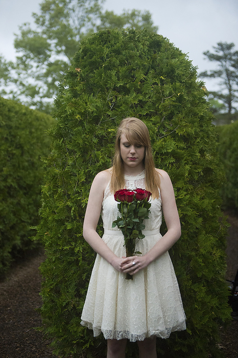 Young woman stands with bouquet of red roses in a garden area; Luray, Virginia, United States of America, by Joel Sartore Photography / Design Pics