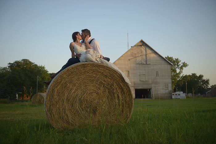 Newlywed couple sharing a kiss on a farm while sitting on a hay bale; Genoa, Nebraska, United States of America, by Joel Sartore Photography / Design Pics