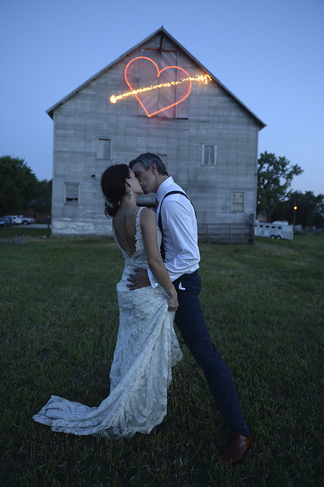 Embracing newlywed couple kissing in front of barn with heart shape made from light trail; Genoa, Nebraska, United States of America, by Joel Sartore Photography / Design Pics
