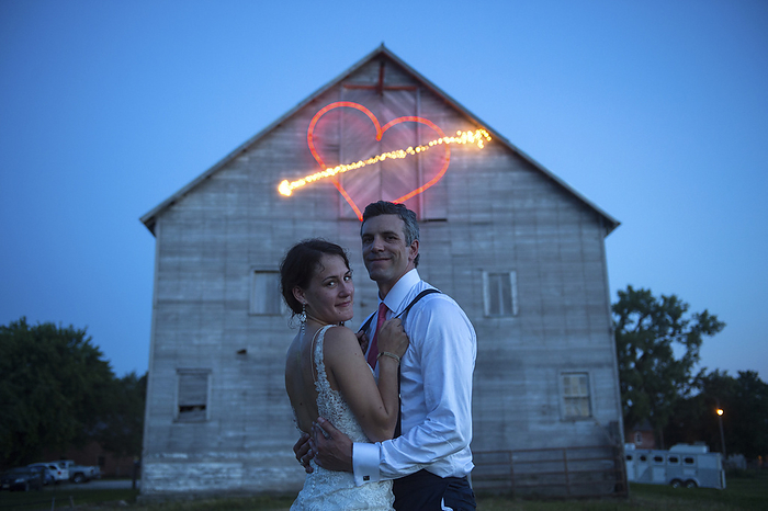 Embracing newlywed couple in front of barn with heart shape made from light trail; Genoa, Nebraska, United States of America, by Joel Sartore Photography / Design Pics