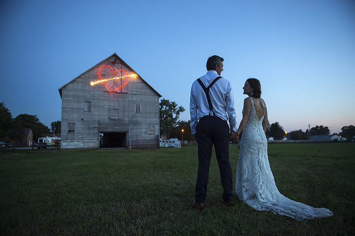 Newlywed couple holding hands in front of barn with heart shape made from light trail; Genoa, Nebraska, United States of America, by Joel Sartore Photography / Design Pics